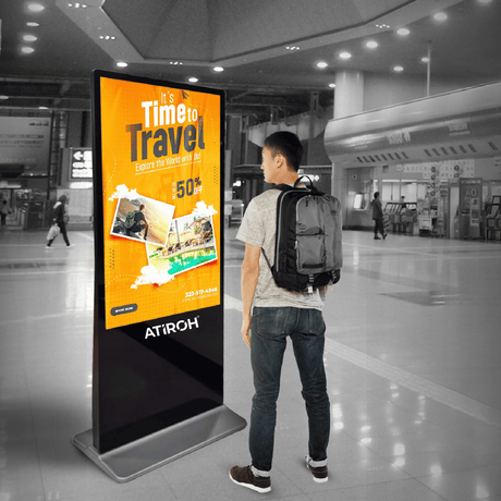 Atiroh indoor digital kiosk displaying a travel advertisement with a man viewing the screen in a modern indoor environment.