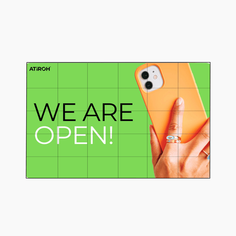 Atiroh video wall displaying “WE ARE OPEN!” message on a bright green background with a hand holding an orange smartphone.